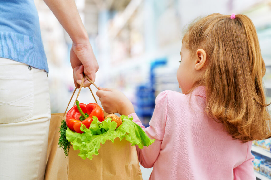 Parent and child holding a shopping bag with fruit & vegetables.