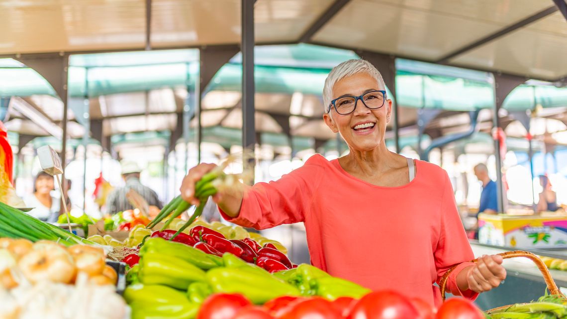 Beautiful senior woman buying vegetables at a farmers market. Woman on greenmarket. Senior woman picking fresh produce at the market. Farmers Market Shopping Mature Woman
